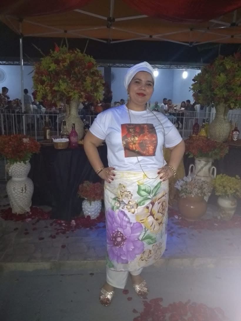 Mãe de santo do Canto da Oxum em uma festa de orixá, de branco e saia florida, com o salão decorado ao fundo